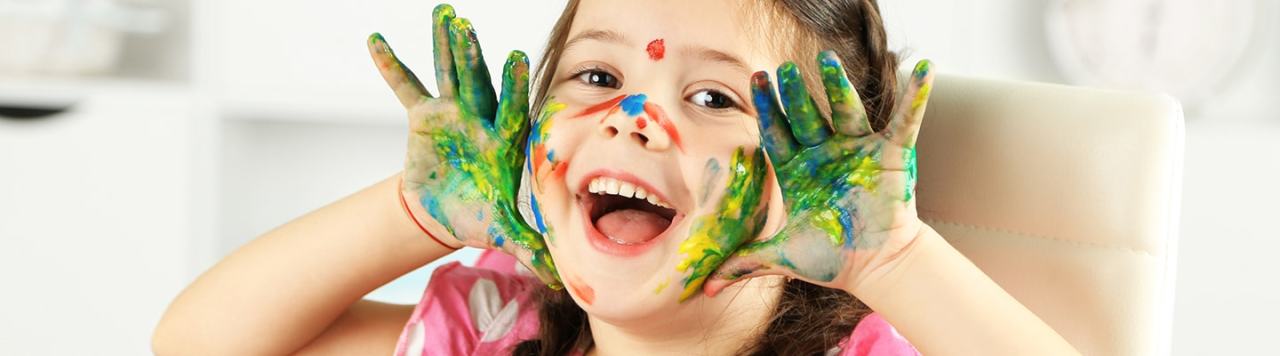 Girl pulling faces with paint stains on her hands and face.