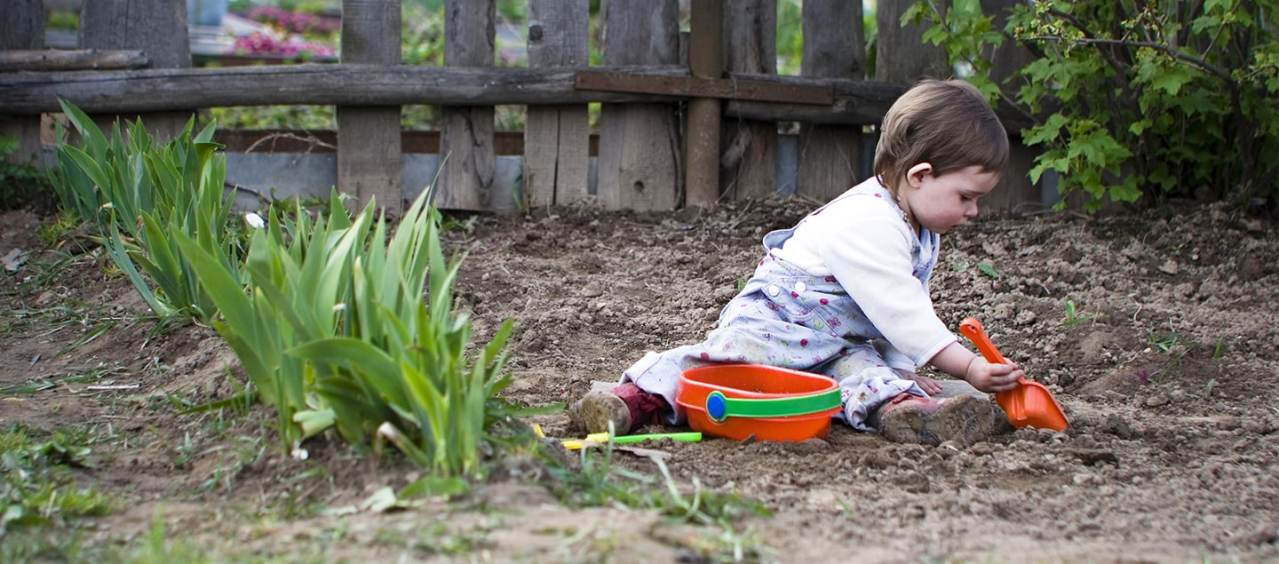 A child playing in mud using a bucket and spade.