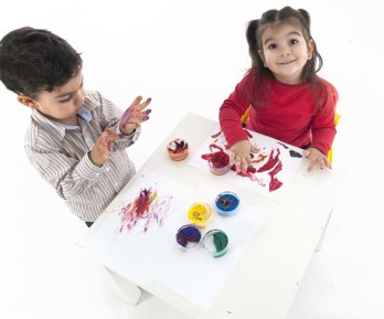nena y nene pintando con las manos con pinturas de colores sobre hojas blancas