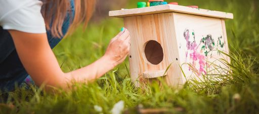 A woman painting a bird box outdoors.