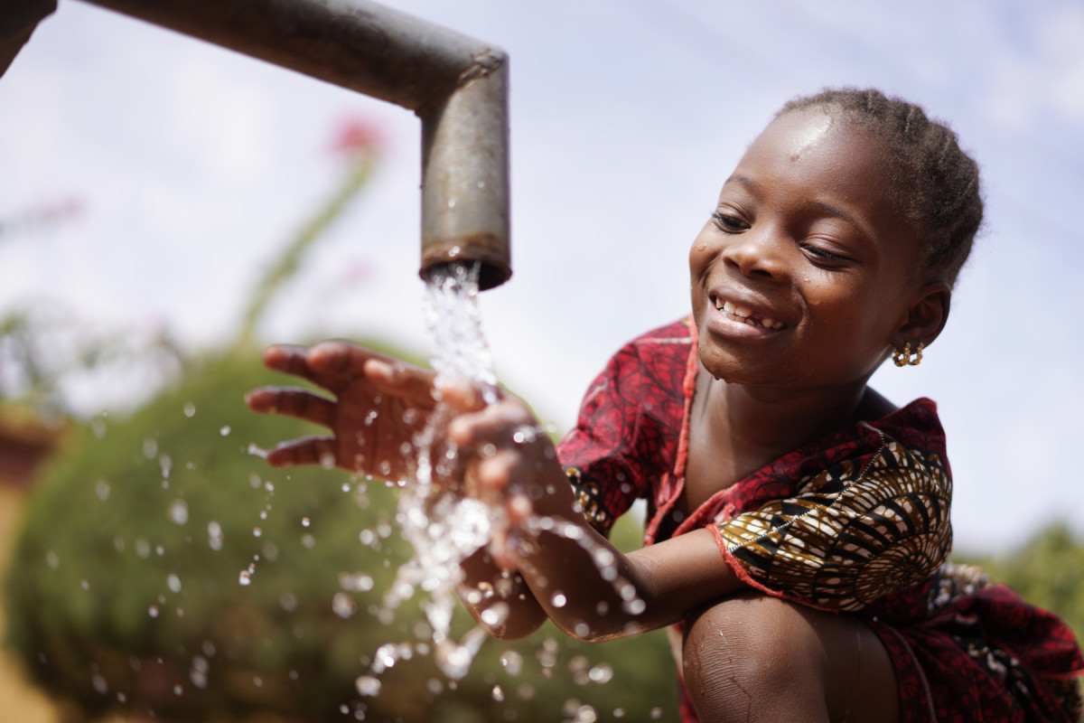 Little child laughing whilst playing with a running water tap