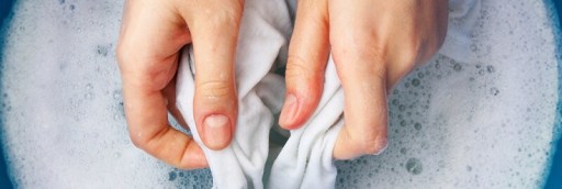 Hand washing clothes in bucket of soapy water