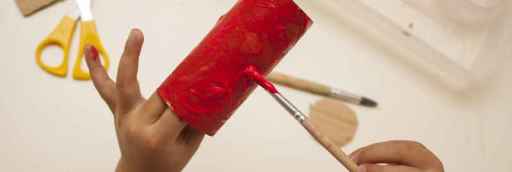 kid painting a toilet roll with red paint