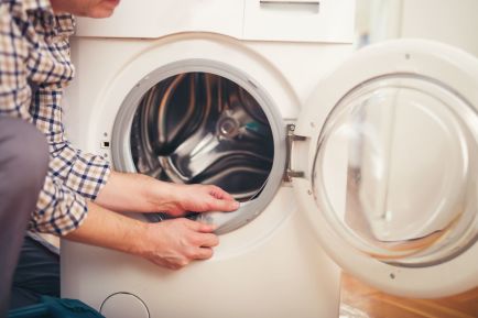 Um homem olhando para o acúmulo de calcário na vedação da porta de uma máquina de lavar