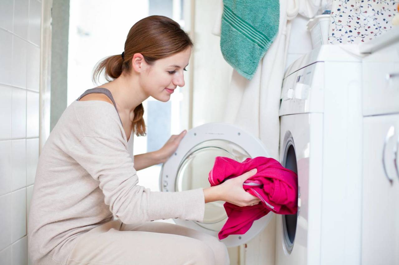 Uma mulher colocando roupas rosa choque na máquina de lavar.
