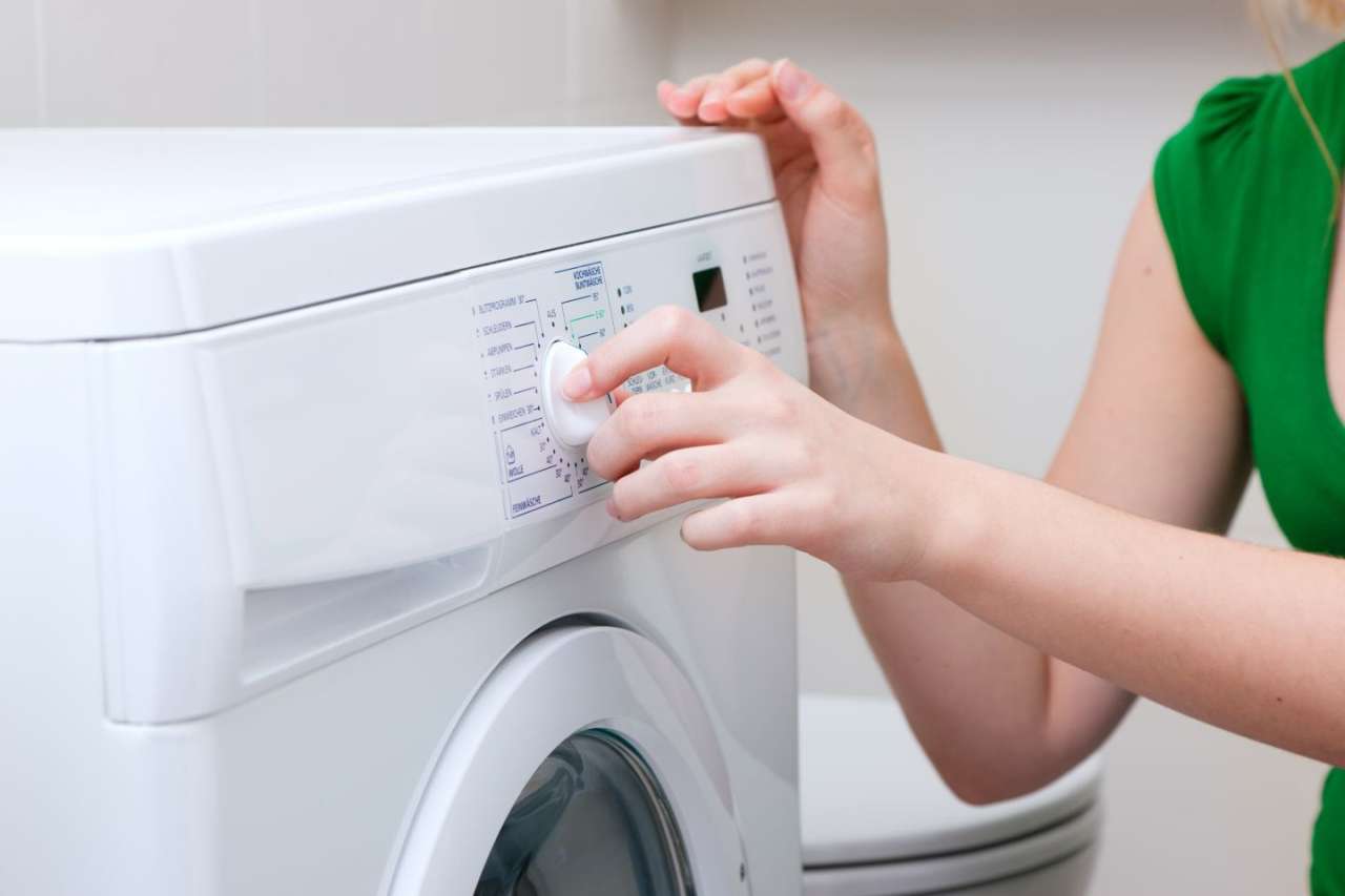 Woman in green top adjusting the settings dial on a washing machine.