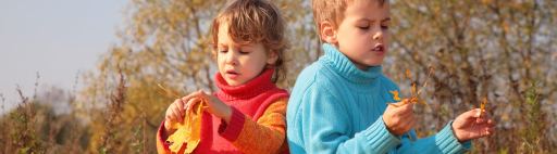 A boy and a girl playing with autumn leaves.