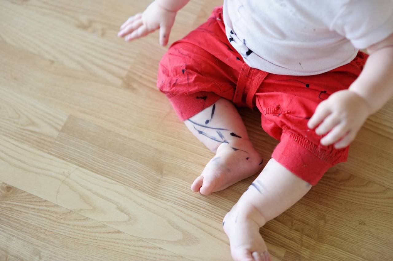 Pernas e roupas de um bebê cobertas de manchas de caneta.