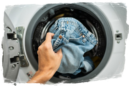 Kot pantolonu çamaşır makinesi tamburuna koyan kişi
