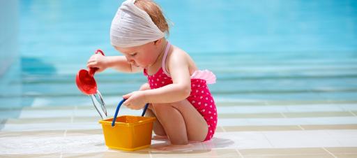 A girl playing with water near a swimming pool using a bucket and ladle.