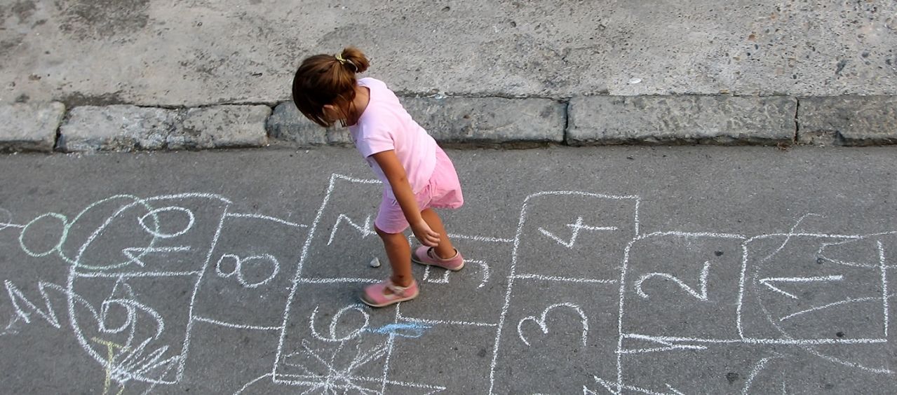 Little girl playing hopscotch in the street.