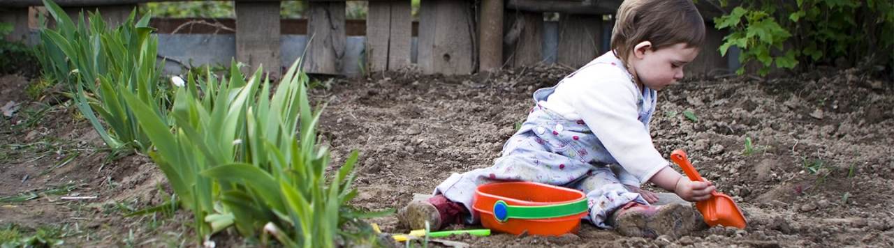A child playing with mud in a garden.