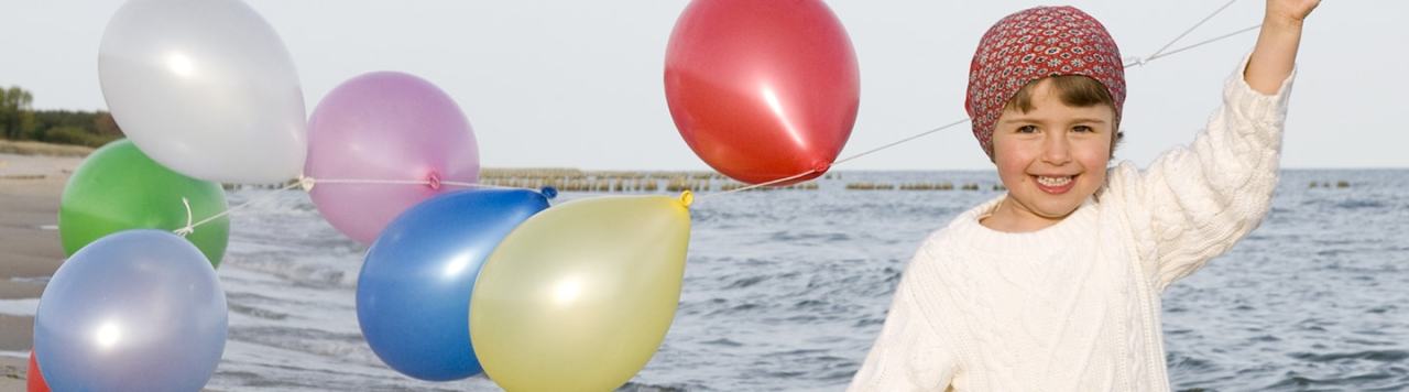 A smiling girl holding colourful balloons near the sea.