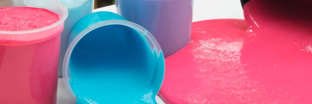 Brightly coloured homemade slime. Multiple containers, some spilt on table, selective focus on the slime