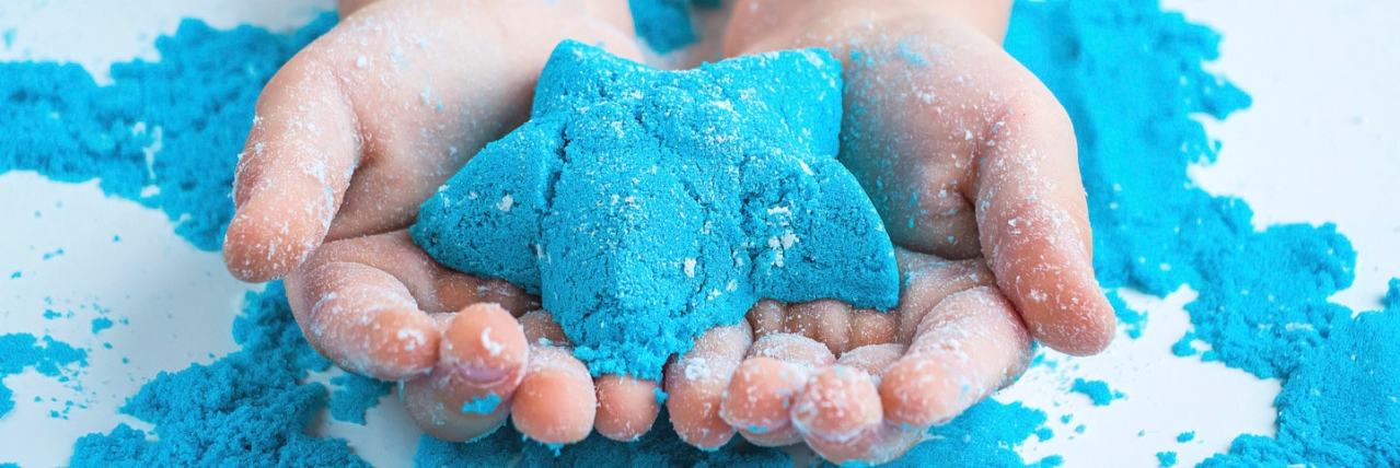 Close up of toddler hand holding blue cloud dough shaped into a starfish over a sensory tray